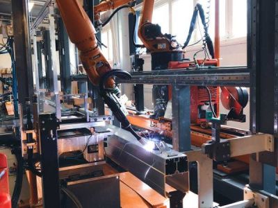 A welding robot at work on a jig holding a clamped workpiece